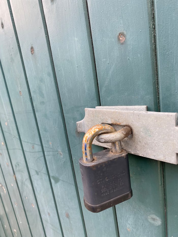 A weathered padlock on a green wooden gate, symbolizing security and protection.